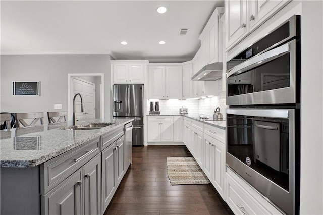 kitchen featuring sink, light stone counters, an island with sink, white cabinets, and appliances with stainless steel finishes