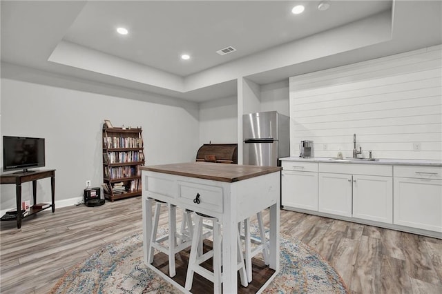 kitchen featuring white cabinets, sink, light wood-type flooring, a tray ceiling, and stainless steel refrigerator