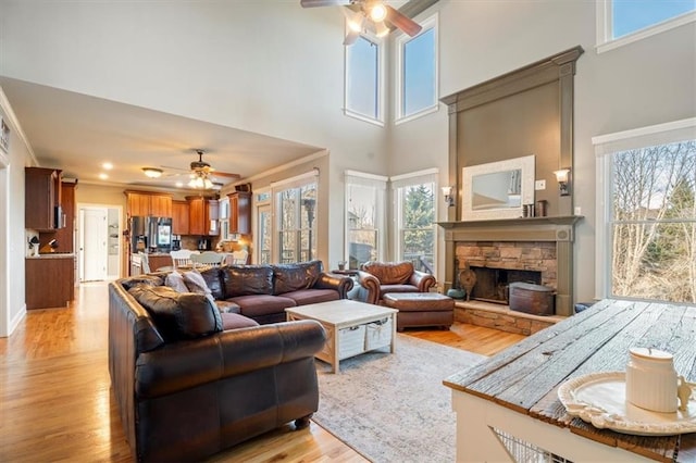 living room featuring ceiling fan, crown molding, a fireplace, and light wood-type flooring