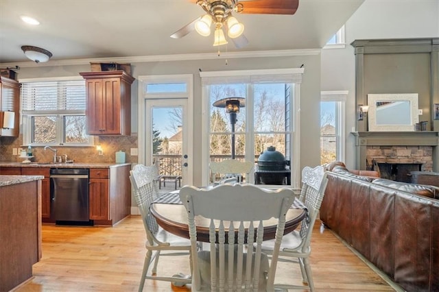 dining room featuring a fireplace, light hardwood / wood-style flooring, ornamental molding, and ceiling fan