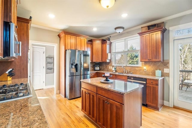 kitchen featuring sink, crown molding, stainless steel appliances, light stone countertops, and a kitchen island