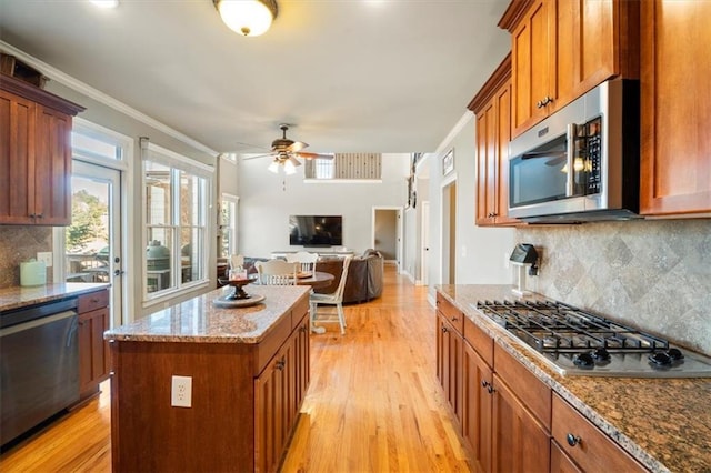 kitchen featuring a kitchen island, ornamental molding, stainless steel appliances, light stone countertops, and light wood-type flooring