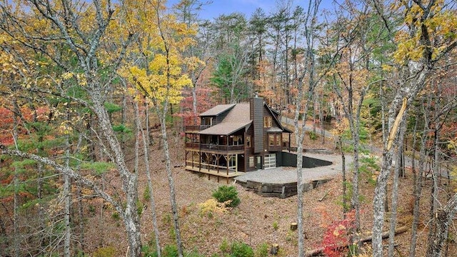 rear view of property featuring driveway, a forest view, a chimney, and a wooden deck