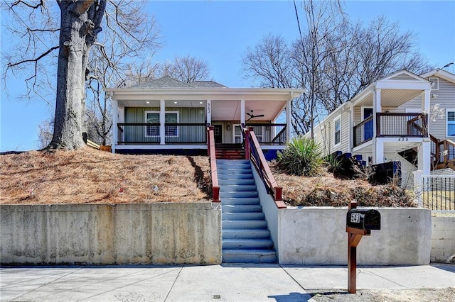 view of front of house with a shingled roof, covered porch, fence, and stairs