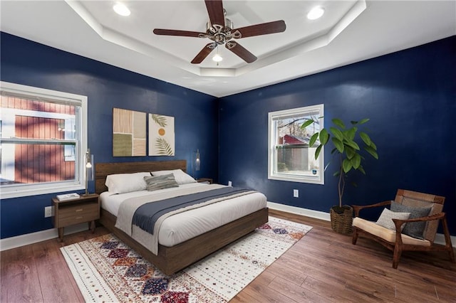 bedroom with hardwood / wood-style flooring, ceiling fan, and a tray ceiling