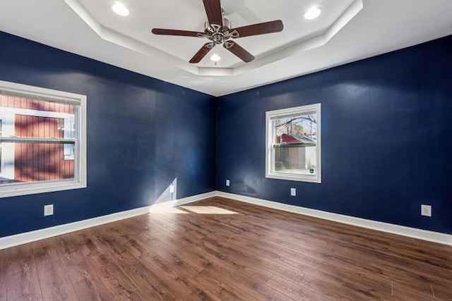 empty room with ceiling fan, wood-type flooring, and a raised ceiling