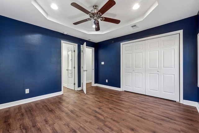 unfurnished bedroom with a raised ceiling, dark hardwood / wood-style floors, ceiling fan, and a closet