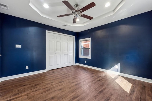 unfurnished bedroom with a raised ceiling, dark hardwood / wood-style floors, ceiling fan, and a closet