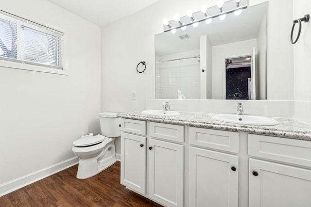 bathroom with wood-type flooring, tiled shower, vanity, and toilet