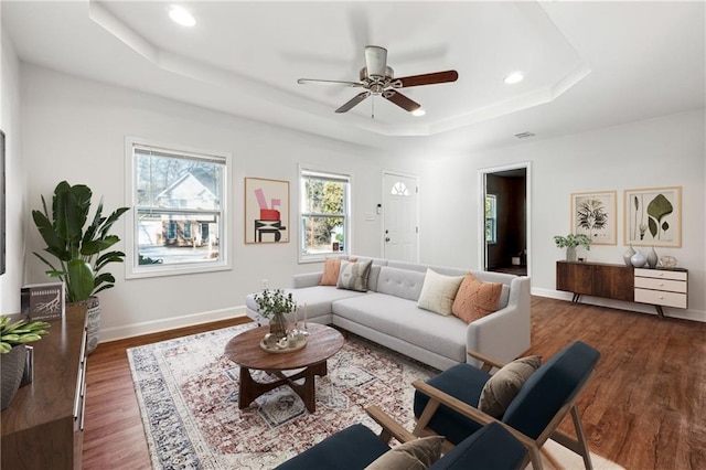 living room featuring dark hardwood / wood-style floors, ceiling fan, and a tray ceiling