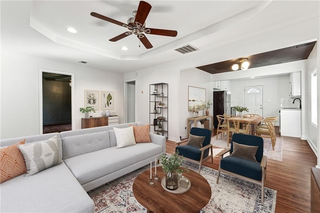 living room with dark hardwood / wood-style floors, a raised ceiling, and ceiling fan