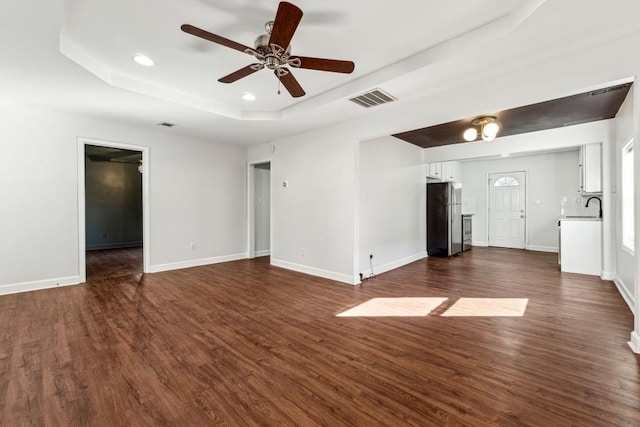 unfurnished living room featuring a raised ceiling, dark hardwood / wood-style floors, sink, and ceiling fan