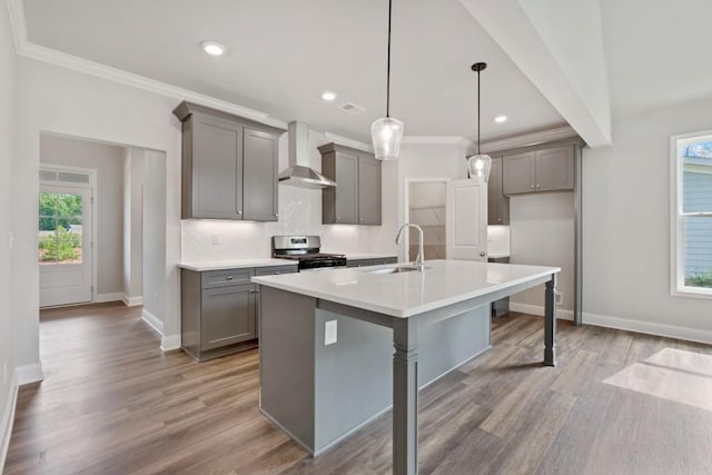 kitchen featuring a breakfast bar, gray cabinets, wall chimney range hood, stainless steel gas stove, and hanging light fixtures