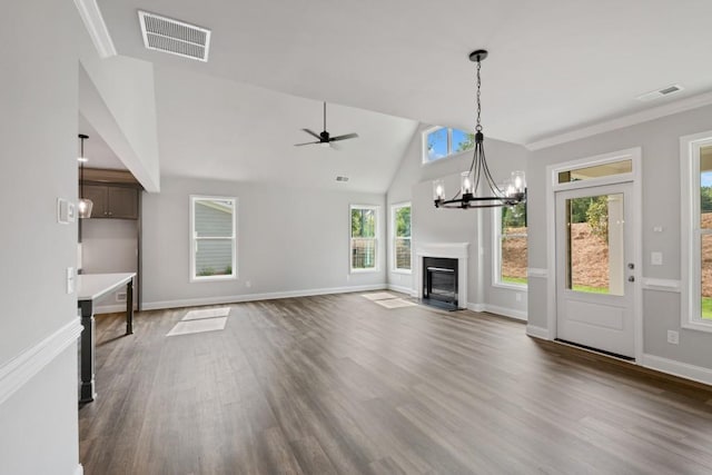 unfurnished living room featuring dark wood-type flooring, vaulted ceiling, crown molding, and ceiling fan with notable chandelier