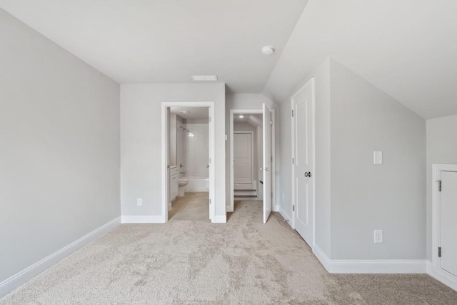 unfurnished bedroom featuring light carpet, lofted ceiling, and ensuite bath