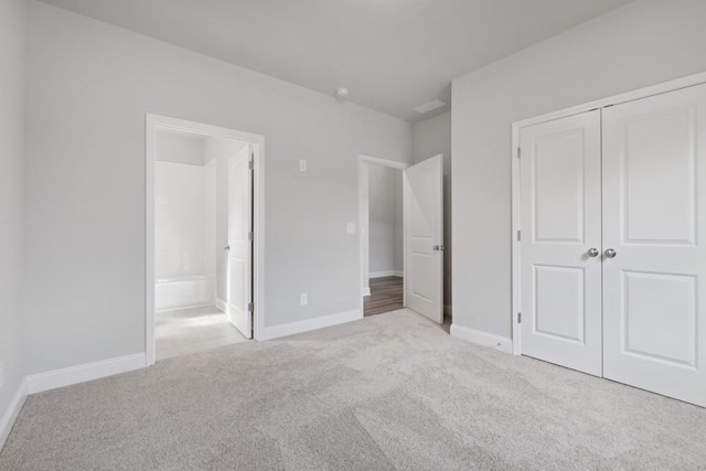 unfurnished bedroom featuring light carpet, ensuite bathroom, and a closet