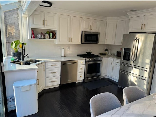 kitchen with premium appliances, white cabinets, sink, light stone counters, and a breakfast bar