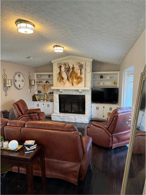 living room featuring a textured ceiling, lofted ceiling, built in shelves, wood-type flooring, and a stone fireplace