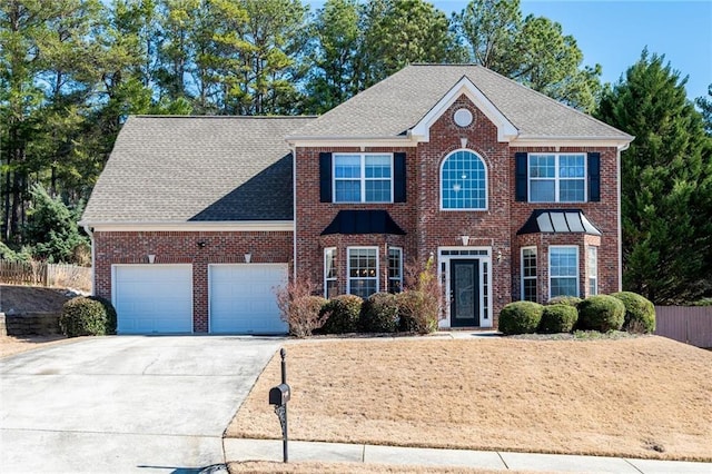 colonial inspired home with a garage, brick siding, a shingled roof, fence, and concrete driveway