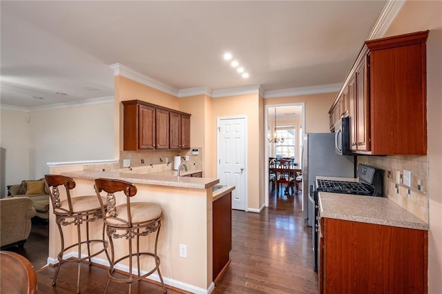 kitchen featuring dark wood-style floors, stainless steel microwave, a breakfast bar, ornamental molding, and gas range oven