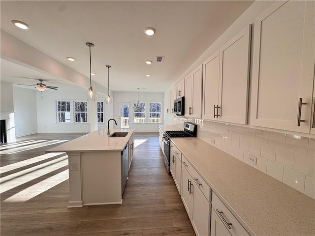 kitchen with sink, a kitchen island with sink, pendant lighting, decorative backsplash, and appliances with stainless steel finishes