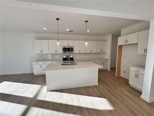 kitchen with a center island with sink, white cabinetry, stainless steel appliances, and hanging light fixtures