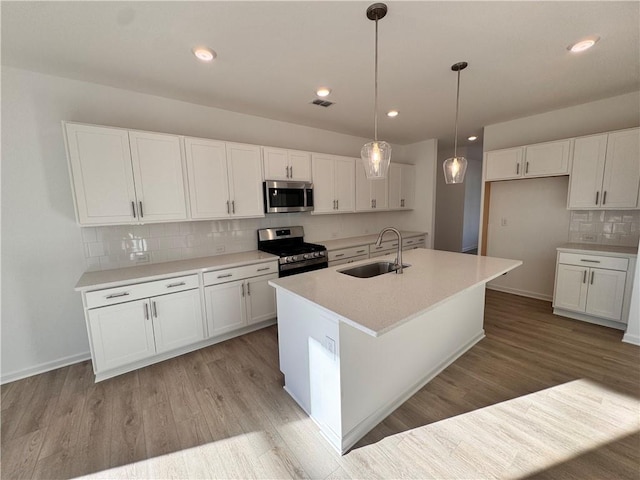 kitchen featuring a kitchen island with sink, sink, decorative light fixtures, white cabinetry, and stainless steel appliances