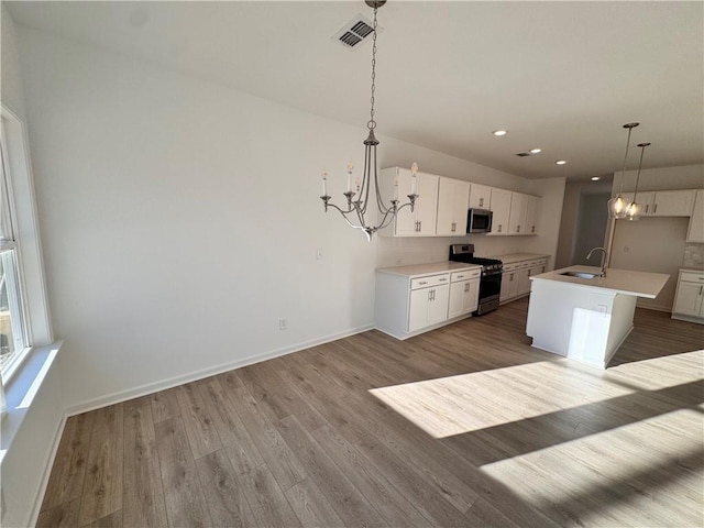 kitchen with hanging light fixtures, white cabinetry, a center island with sink, and stainless steel appliances