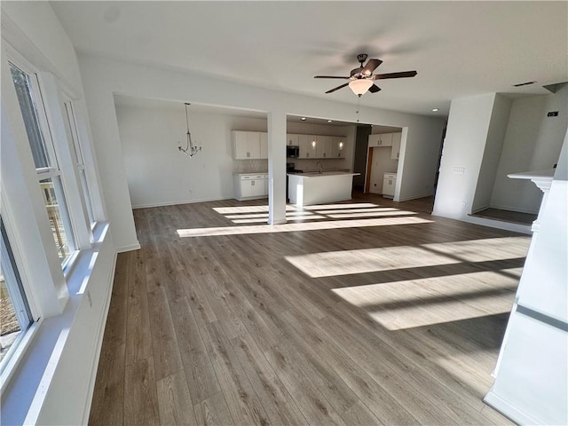 unfurnished living room with hardwood / wood-style floors, ceiling fan with notable chandelier, and sink