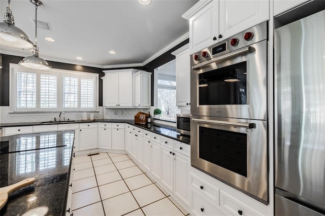 kitchen with appliances with stainless steel finishes, white cabinetry, backsplash, decorative light fixtures, and dark stone counters