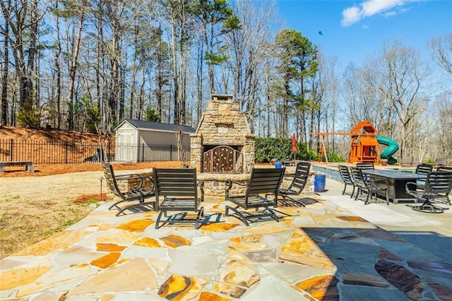 view of patio / terrace with a playground, an outdoor stone fireplace, and a storage shed