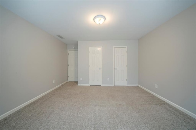 unfurnished bedroom featuring baseboards, visible vents, multiple closets, and light colored carpet