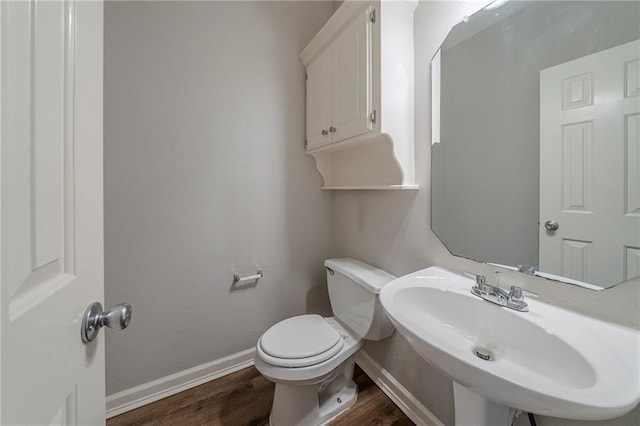 half bathroom featuring baseboards, a sink, toilet, and wood finished floors