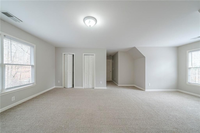 unfurnished bedroom featuring baseboards, visible vents, two closets, and light colored carpet