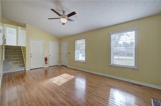 empty room featuring light wood-type flooring, a textured ceiling, and vaulted ceiling