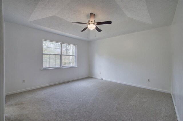 carpeted empty room with a textured ceiling, ceiling fan, and a tray ceiling