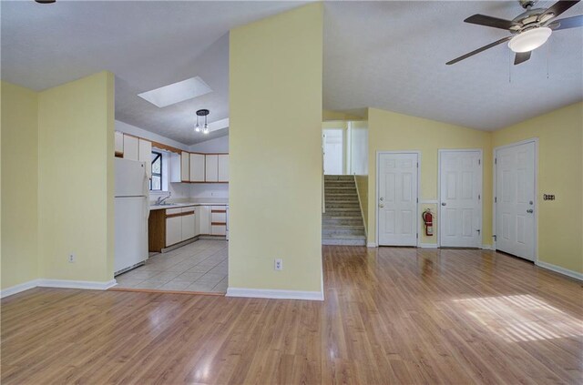 unfurnished living room featuring lofted ceiling with skylight, ceiling fan, sink, and light hardwood / wood-style floors