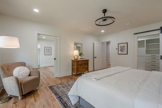bedroom featuring a barn door, recessed lighting, light wood finished floors, a walk in closet, and baseboards