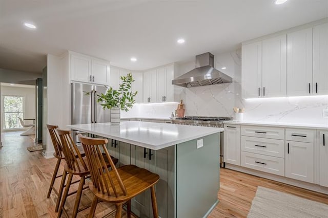 kitchen with light wood-style flooring, white cabinets, wall chimney range hood, a kitchen island, and tasteful backsplash