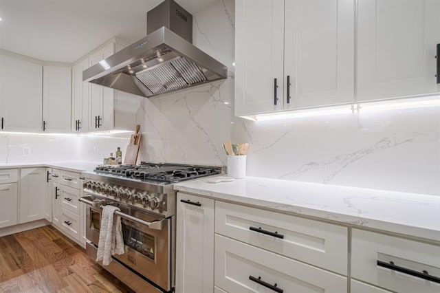 kitchen with light wood-type flooring, wall chimney range hood, white cabinetry, and double oven range