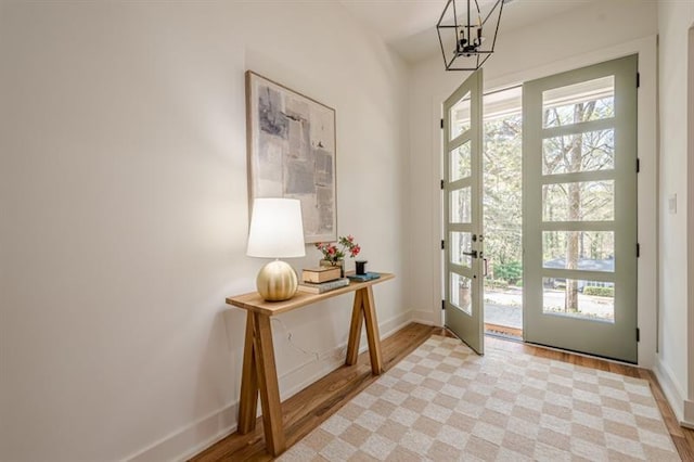 entryway with an inviting chandelier, baseboards, french doors, and light wood-style floors