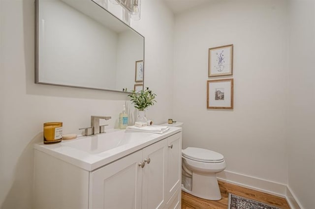 half bathroom featuring toilet, baseboards, wood finished floors, and vanity