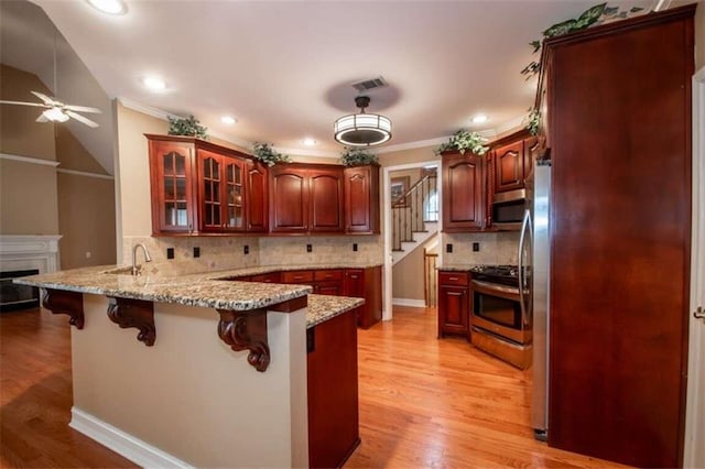 kitchen featuring ceiling fan, light wood-type flooring, appliances with stainless steel finishes, kitchen peninsula, and a breakfast bar area