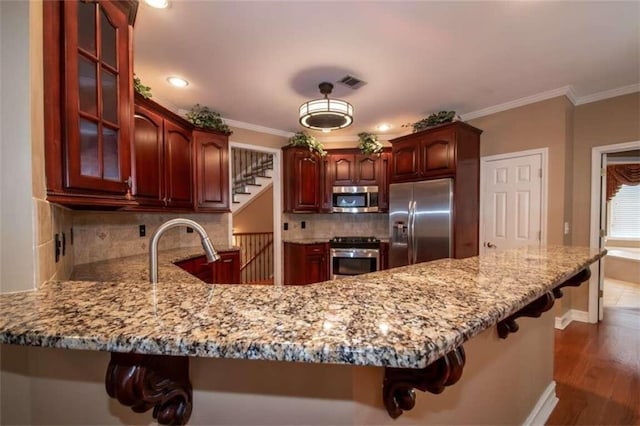 kitchen featuring kitchen peninsula, a kitchen bar, ornamental molding, stainless steel appliances, and dark wood-type flooring