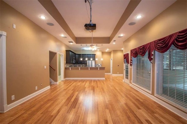 unfurnished living room with ceiling fan, a raised ceiling, and light hardwood / wood-style flooring