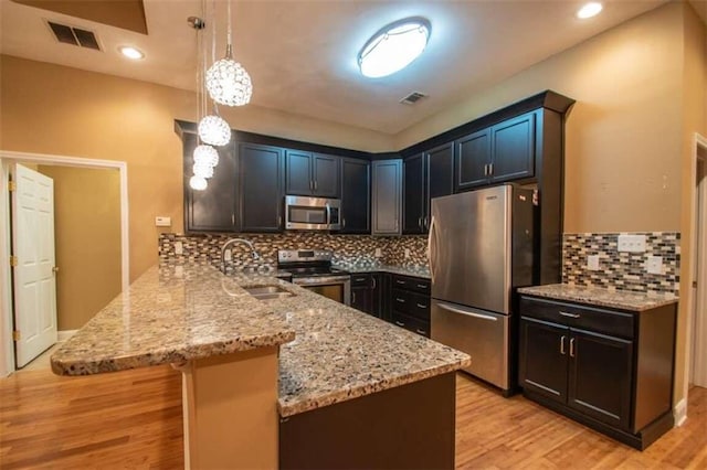 kitchen featuring sink, stainless steel appliances, light hardwood / wood-style flooring, kitchen peninsula, and pendant lighting