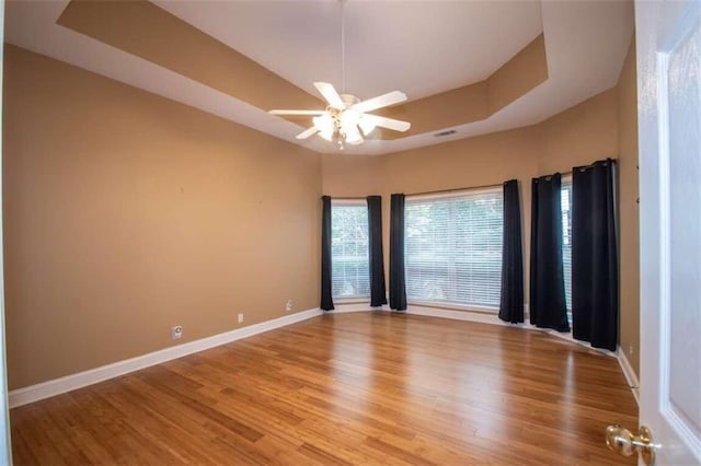 spare room with light hardwood / wood-style floors, ceiling fan, and a tray ceiling