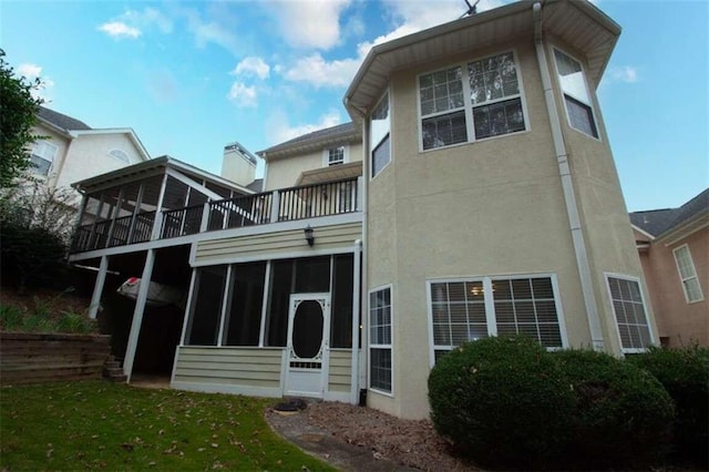 rear view of house with a lawn, a sunroom, and a balcony