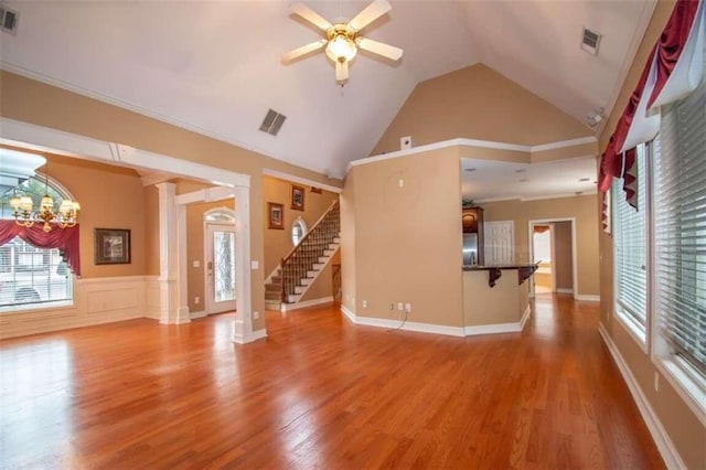 unfurnished living room featuring high vaulted ceiling, ceiling fan with notable chandelier, crown molding, hardwood / wood-style flooring, and decorative columns