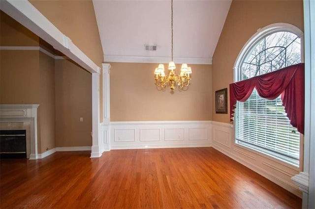 unfurnished dining area featuring high vaulted ceiling, hardwood / wood-style flooring, ornamental molding, a fireplace, and a chandelier